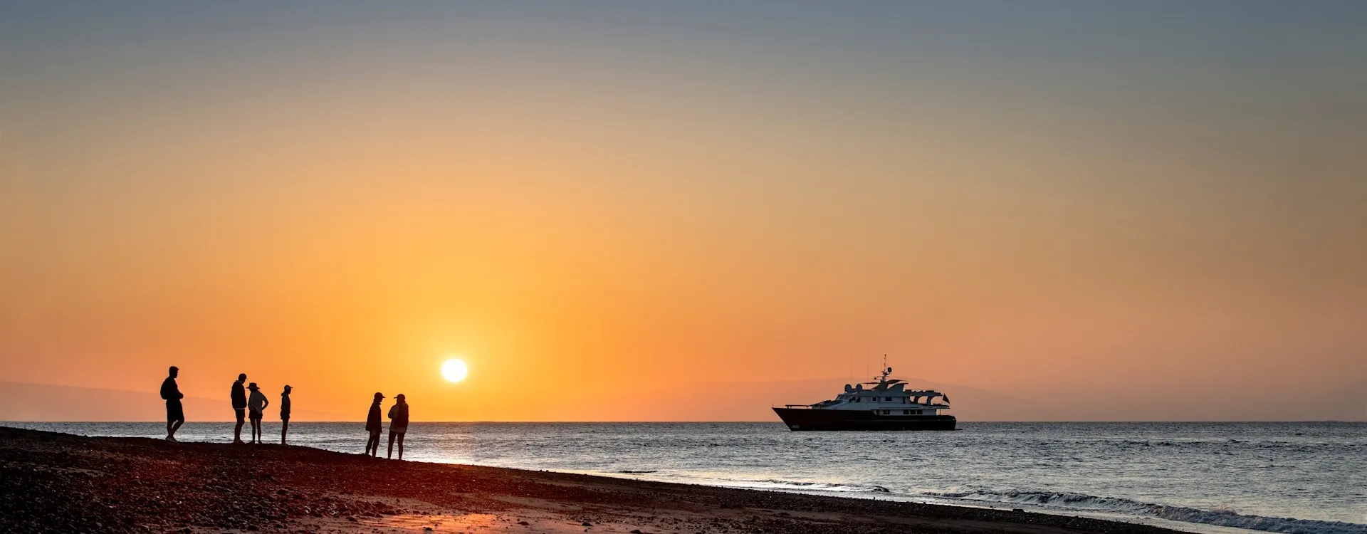 People playing on the beach at sunset with a private yacht in the background